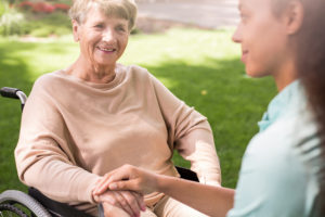 An older woman receiving home care services in Sacramento smiles in her wheelchair as her caregiver stands beside her.