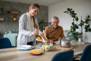 A caregiver serves dinner to an older man whose family caregiver arranged for respite care services.