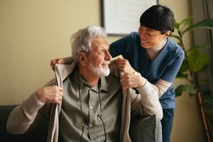 A caregiver providing personal care in Sacramento helps an older man put on a sweater.