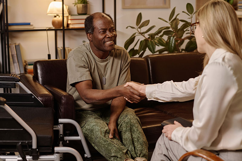 A smiling veteran sits comfortably at home, enjoying a conversation with his caregiver.