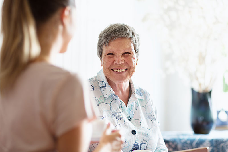 An older woman smiles as she talks with her Chico caregiver.