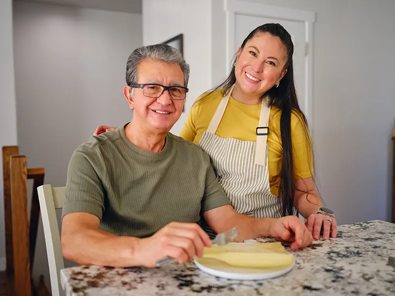 A home care caregiver in Auburn smiles as she serves a meal to an older man.