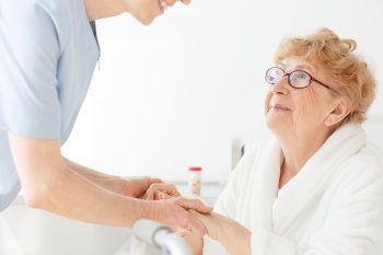 An older woman receives help with senior recovery after hospitalization from a caregiver.